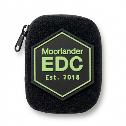 Black Cordura micro EDC pouch with hook and loop front panel featuring a black and neon green Moorlander EDC hexagon PVC patch, front facing on a white background.
